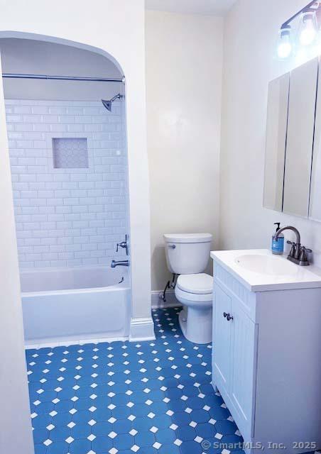 bathroom featuring toilet, vanity, tub / shower combination, tile patterned floors, and baseboards