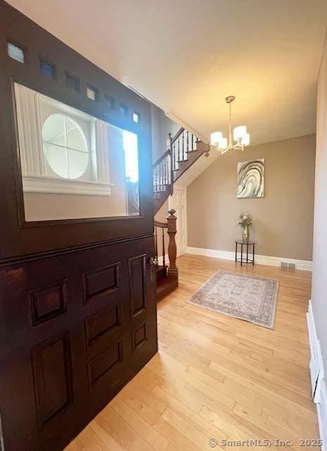 entrance foyer featuring stairway, light wood finished floors, a chandelier, and baseboards
