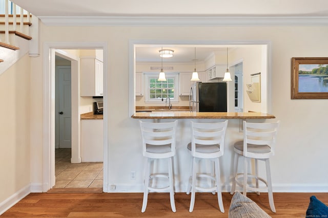 94 Mulberry St, Stamford, CT 06907 - kitchen with freestanding refrigerator, white cabinetry, crown molding, wood finished floors, and a kitchen breakfast bar