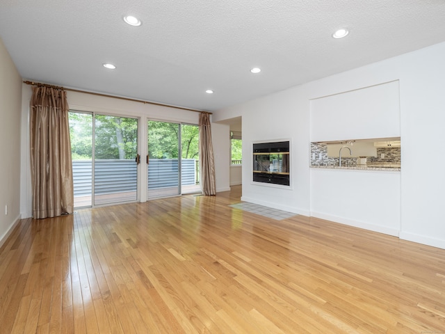 24 Wilton Crst Unit 24, Wilton, CT 06897 - unfurnished living room with light wood finished floors, a sink, a multi sided fireplace, recessed lighting, and a textured ceiling