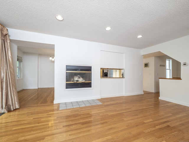 24 Wilton Crst Unit 24, Wilton, CT 06897 - unfurnished living room featuring light wood-style floors, a multi sided fireplace, a textured ceiling, recessed lighting, and baseboards