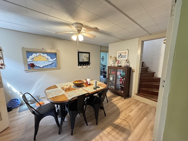 dining area featuring light wood-style flooring, a ceiling fan, and stairs