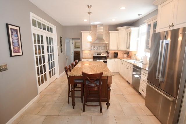 27 Regency Dr, North Haven, CT 06473 - kitchen featuring appliances with stainless steel finishes, wall chimney exhaust hood, backsplash, light stone countertops, and decorative light fixtures
