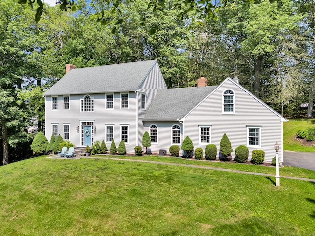 27 Regency Dr, North Haven, CT 06473 - colonial-style house featuring a chimney, a front lawn, a shingled roof, and view of scattered trees