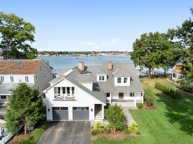 view of front facade featuring driveway, a water view, a chimney, an attached garage, and a front yard