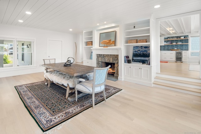 dining room with wood finished floors, wine cooler, a stone fireplace, wood ceiling, and recessed lighting