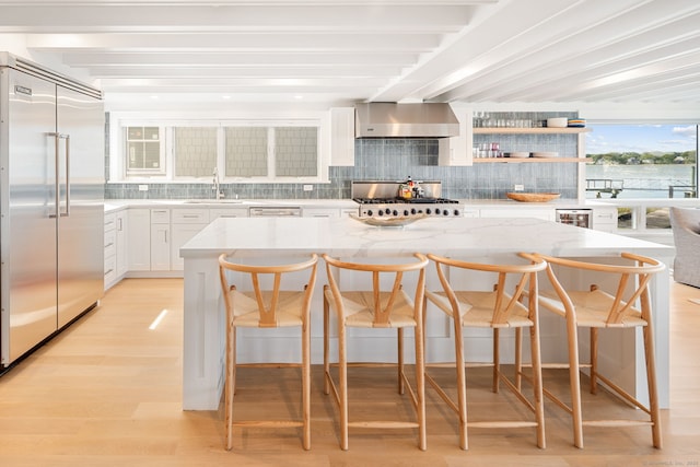 kitchen with built in fridge, wall chimney range hood, decorative backsplash, a sink, and light stone counters
