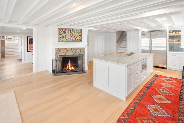 kitchen with built in appliances, beam ceiling, light wood finished floors, white cabinets, and light stone countertops