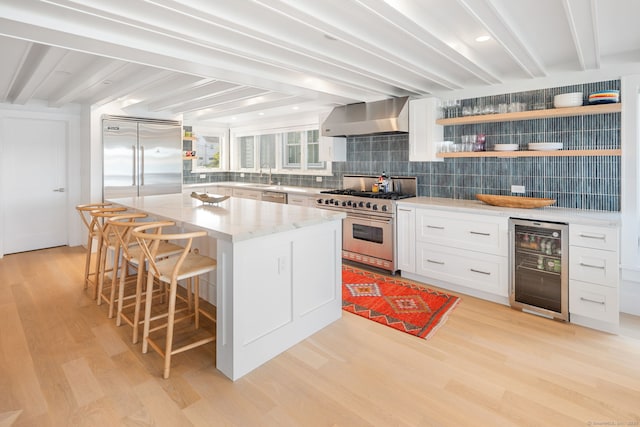 kitchen featuring high quality appliances, wine cooler, wall chimney range hood, a sink, and backsplash