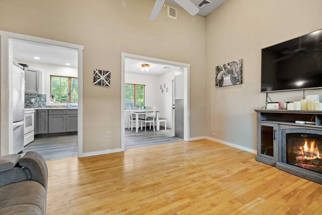 11 Osprey Ln, East Lyme, CT 06357 - living room with light wood-style floors, a warm lit fireplace, baseboards, a ceiling fan, and a towering ceiling