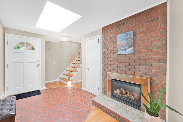 entrance foyer featuring stairway, a skylight, wood finished floors, a fireplace, and baseboards