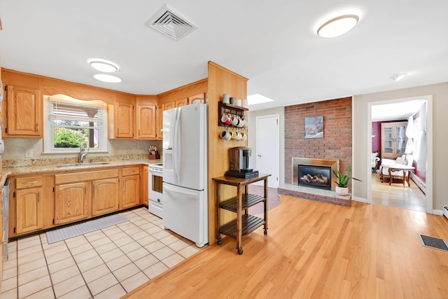 kitchen with white appliances, a sink, light wood-style flooring, a brick fireplace, and a baseboard radiator