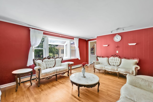 living area featuring baseboard heating, ornamental molding, wood finished floors, baseboards, and track lighting