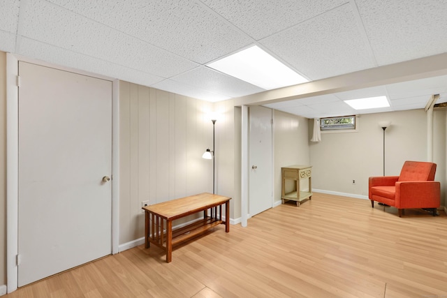 living area with a paneled ceiling, light wood-style flooring, and baseboards