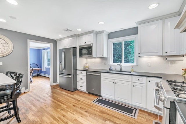 kitchen featuring appliances with stainless steel finishes, a sink, dark countertops, light wood-type flooring, and recessed lighting