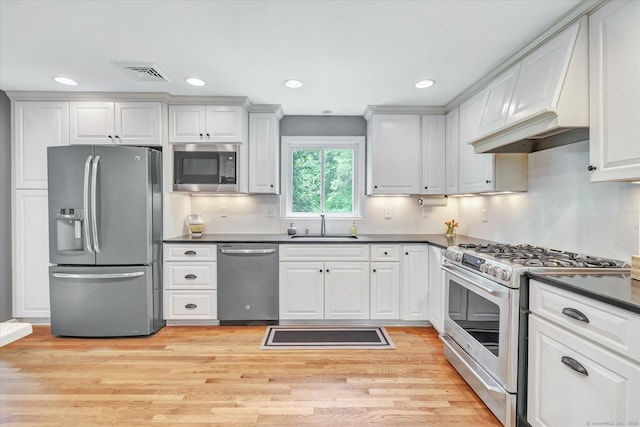 kitchen featuring appliances with stainless steel finishes, dark countertops, a sink, light wood finished floors, and recessed lighting