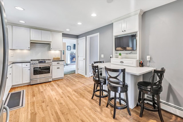 kitchen featuring stainless steel appliances, white cabinets, light wood-type flooring, a kitchen breakfast bar, and recessed lighting