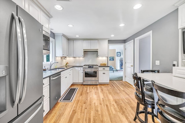 kitchen featuring stainless steel appliances, a sink, light wood-style floors, recessed lighting, and white cabinets