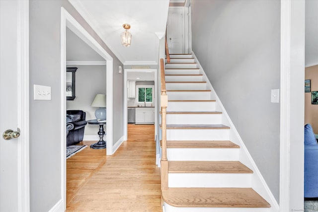 staircase featuring wood finished floors, ornamental molding, and baseboards
