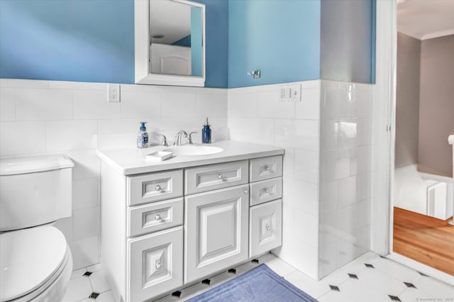 bathroom with tile walls, toilet, vanity, tile patterned floors, and a wainscoted wall
