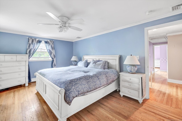 bedroom with light wood finished floors, crown molding, a ceiling fan, baseboards, and attic access