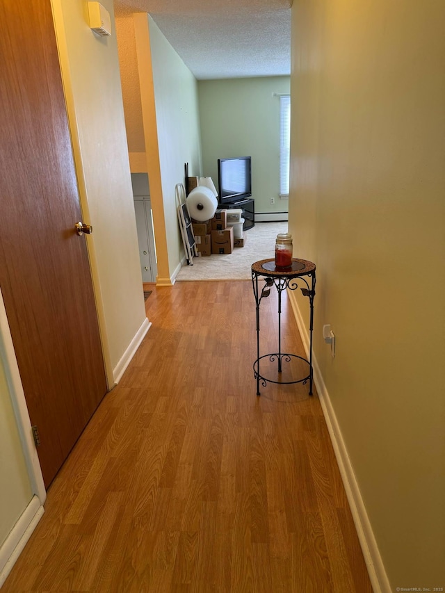 corridor with wood finished floors, a baseboard heating unit, and baseboards
