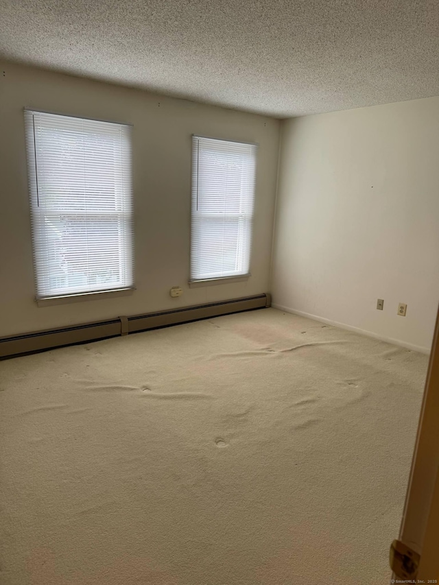 empty room with a textured ceiling, healthy amount of natural light, carpet, a baseboard radiator, and baseboards