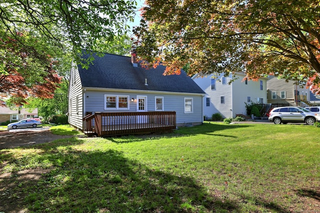 rear view of property with a chimney, a lawn, a deck, and a shingled roof