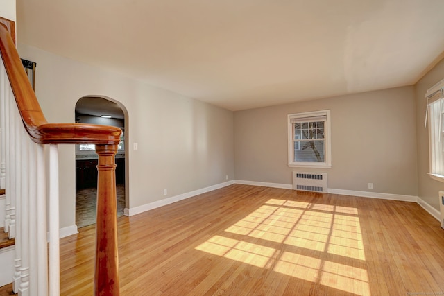 unfurnished living room featuring radiator, arched walkways, light wood-style floors, and baseboards