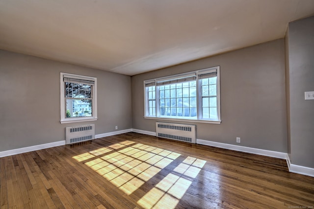 empty room with radiator heating unit, hardwood / wood-style flooring, and baseboards