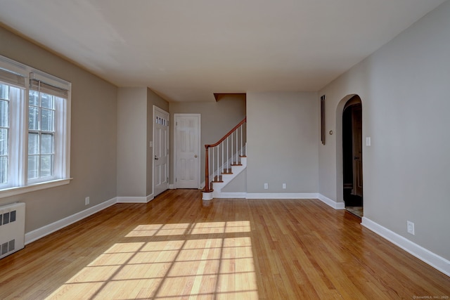 spare room featuring light wood-style floors, arched walkways, radiator heating unit, baseboards, and stairs