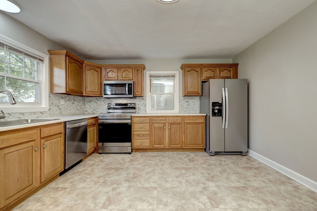kitchen with appliances with stainless steel finishes, a sink, light countertops, decorative backsplash, and brown cabinetry