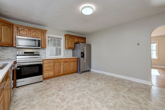kitchen featuring appliances with stainless steel finishes, arched walkways, decorative backsplash, and light countertops