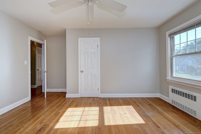 spare room featuring radiator, light wood-style floors, baseboards, and a ceiling fan