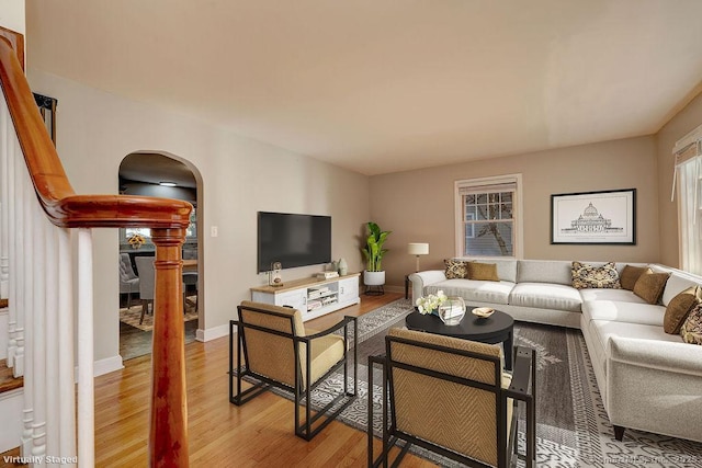 living area with arched walkways, light wood-type flooring, and baseboards