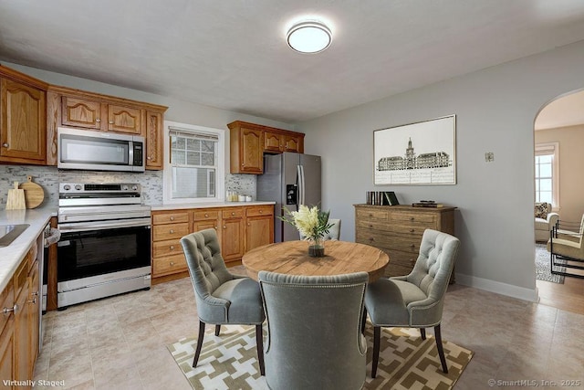 kitchen with appliances with stainless steel finishes, arched walkways, light countertops, and tasteful backsplash