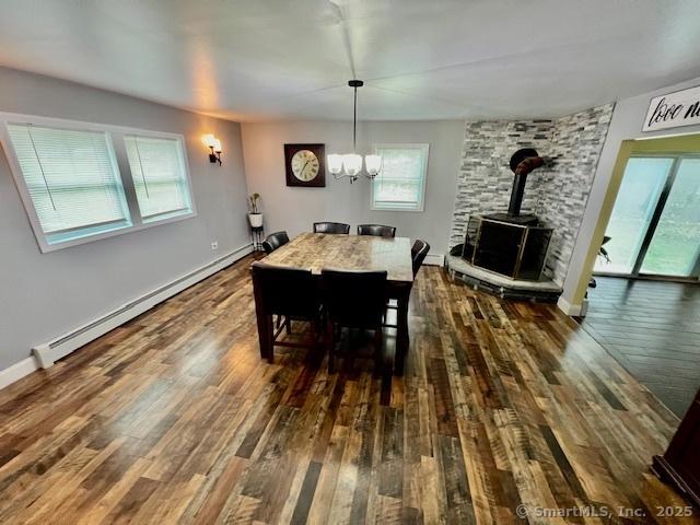 dining area featuring a wood stove, baseboard heating, wood finished floors, and a chandelier