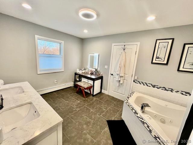 bathroom with a baseboard radiator, double vanity, a whirlpool tub, and baseboards