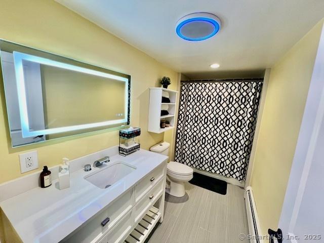 bathroom featuring a baseboard radiator, toilet, vanity, and curtained shower