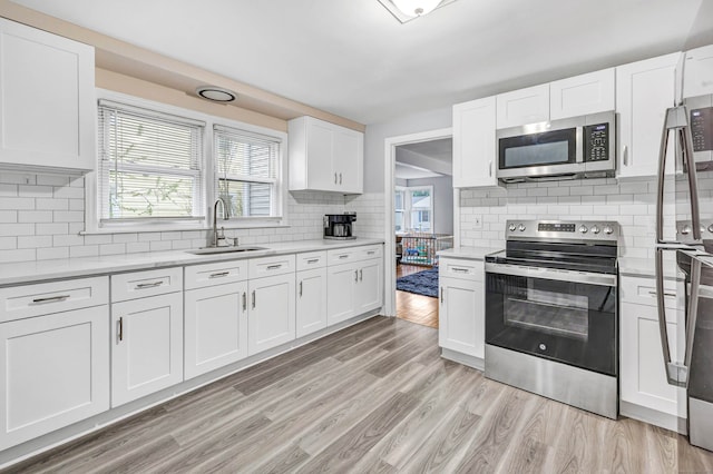 592 Courtland Ave, Bridgeport, CT 06605 - kitchen featuring appliances with stainless steel finishes, a sink, decorative backsplash, white cabinets, and light wood-type flooring