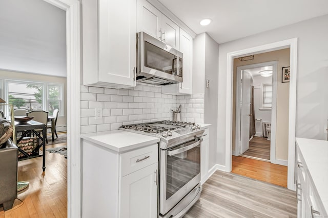 592 Courtland Ave, Bridgeport, CT 06605 - kitchen with appliances with stainless steel finishes, light countertops, light wood-style flooring, white cabinets, and backsplash