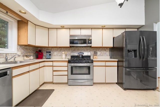 kitchen with stainless steel appliances, a sink, light countertops, tasteful backsplash, and light flooring