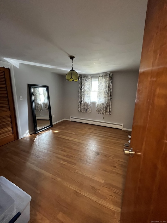 empty room with a baseboard heating unit, baseboards, and wood finished floors