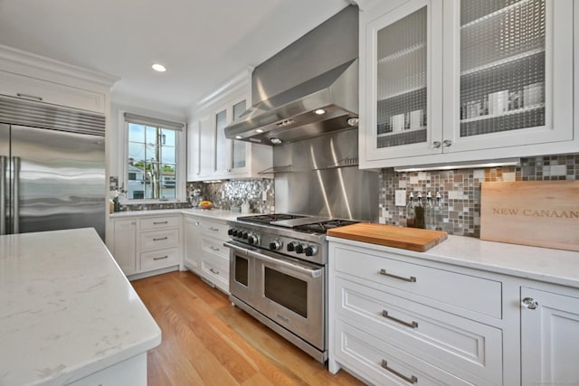 144 S Ave, New Canaan, CT 06840 - kitchen with high end appliances, wall chimney range hood, white cabinetry, light wood finished floors, and recessed lighting