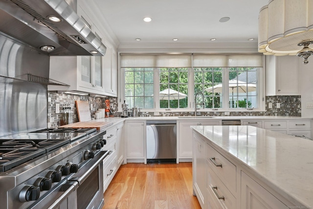 144 S Ave, New Canaan, CT 06840 - kitchen featuring wall chimney exhaust hood, stainless steel appliances, a sink, white cabinetry, and light stone countertops