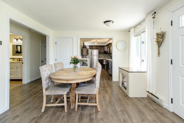 dining area featuring baseboard heating, light wood finished floors, baseboards, and a textured ceiling
