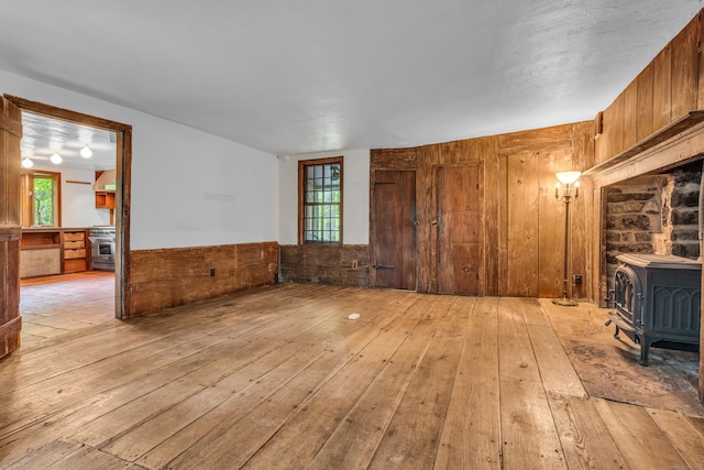 804 Forest Rd, North Branford, CT 06472 - unfurnished living room with light wood-style floors, a wood stove, wooden walls, and a wainscoted wall