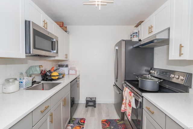 kitchen with appliances with stainless steel finishes, under cabinet range hood, light wood-style flooring, light countertops, and baseboards