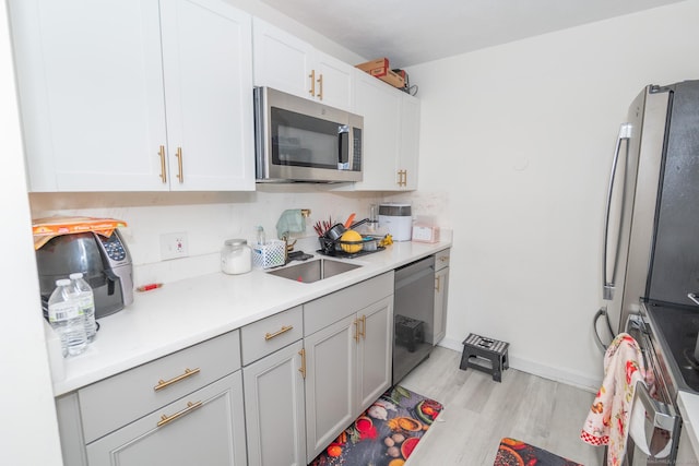 kitchen featuring appliances with stainless steel finishes, a sink, light wood-style floors, light countertops, and white cabinetry