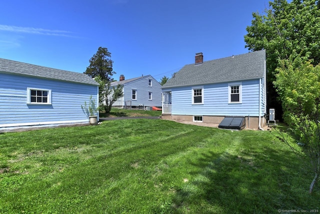 back of house featuring a lawn, a chimney, and a shingled roof